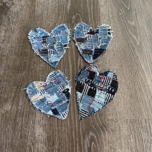 May include: Four heart-shaped denim patches with frayed edges. Each heart is constructed from various denim scraps in shades of blue, black, and white, with hints of red. The patches are arranged on a wooden surface.