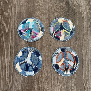 May include: Four denim peace sign patches with colorful patchwork details. Each patch is circular, featuring a peace sign design in various colors like blue, orange, and pink. The patches are arranged on a wooden surface.