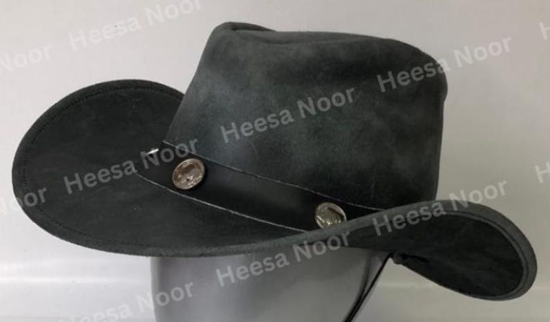 May include: A dark gray cowboy hat with a wide brim and a leather band. The hat features two decorative silver-colored buttons on the band. The hat is made of a soft, suede-like material.