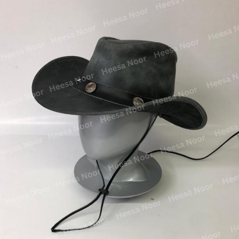 May include: A dark gray cowboy hat with a wide brim and a leather band. The hat is decorated with two silver-colored studs. A black chin strap is attached. The hat is displayed on a mannequin head.