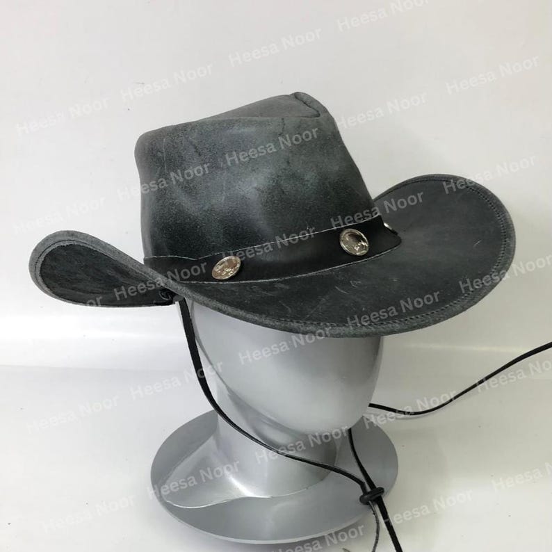 May include: A distressed gray cowboy hat with a black leather band and decorative silver-toned studs. The hat has a wide brim and a chin strap. The hat is displayed on a mannequin head. The hat is approximately 15 inches in diameter.