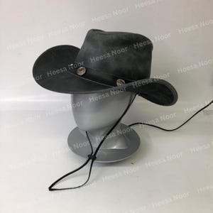 May include: A gray suede cowboy hat with a wide brim and a leather band. The hat features two decorative silver-colored buttons and a chin strap. The hat is displayed on a mannequin head.