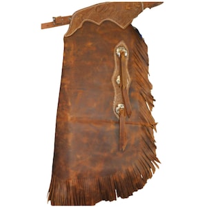 May include: Brown leather chaps with decorative stitching and fringe along the bottom edge. The chaps feature silver-toned hardware and leather straps. The top portion has a decorative embossed design. A classic Western wear item.