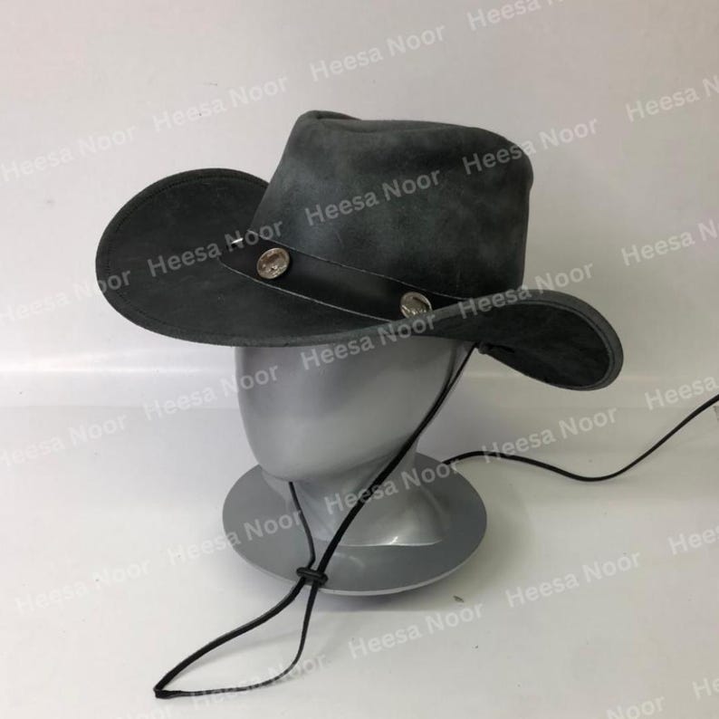 May include: A dark gray cowboy hat with a wide brim and a leather band. The hat is decorated with two silver-colored studs. A black chin strap is attached. The hat is displayed on a mannequin head.
