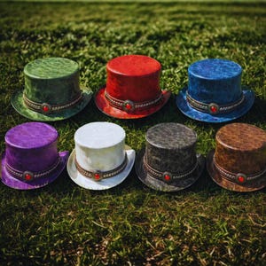 May include: Seven top hats in green, red, blue, purple, white, gray, and brown. Each hat features a textured finish, a braided band, and a central circular ornament with a red stone. The hats are arranged in two rows on a grassy surface.
