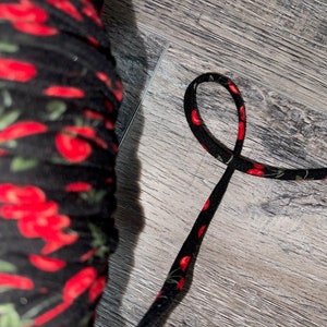 May include: Black elastic with a red cherry print. The elastic is folded in half and is lying on a wood surface.