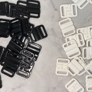 May include: A close-up of two piles of plastic bra clasps. One pile is black and the other is white.