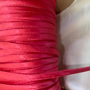 May include: A spool of bright red satin ribbon. The ribbon is wound tightly and is ready to be used for crafting, decorating, or gift wrapping.