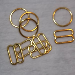 May include: A set of gold-toned metal bra strap adjusters. The set includes four oval-shaped adjusters and two round rings.