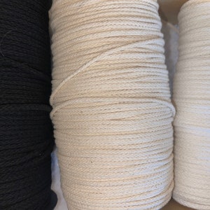 May include: Three spools of cord arranged side by side. The left spool is black, the center spool is a natural beige, and the right spool is white. Each spool is tightly wound with a continuous length of braided cord, showing a consistent texture.