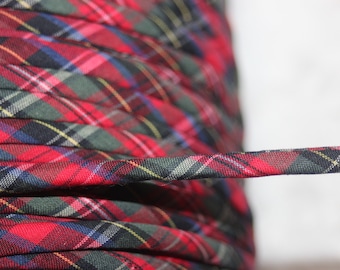 May include: Close-up of a spool of red, green, blue, and yellow plaid fabric trim. The trim is tightly coiled, with a length extending outward. The fabric has a classic tartan pattern.