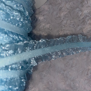 May include: Light blue elastic trim with a sparkly finish. The trim has a ruffled edge and is made of a sheer fabric.