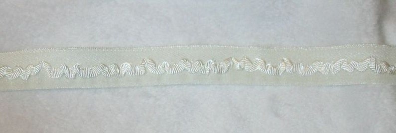 Pode incluir: Fita de cetim branco com um delicado desenho bordado branco de formas de folhas repetidas.