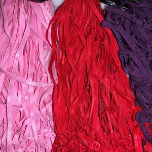 May include: A bundle of pink, red, and purple elastic bra straps. The straps are all the same length and width, and they are arranged in a neat pile.