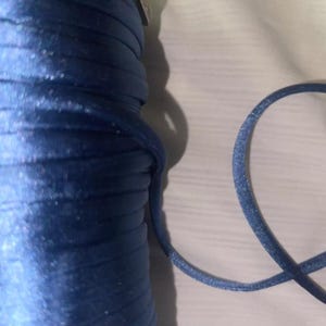 May include: A spool of blue satin cord with a small piece of the cord laying next to it.