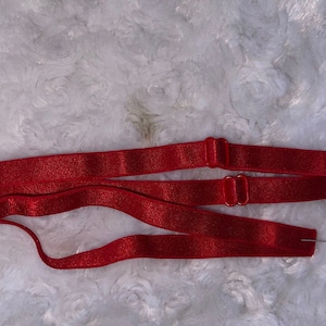 May include: Red bra strap extenders with metal clasps. The extenders are lying on a white fuzzy surface.