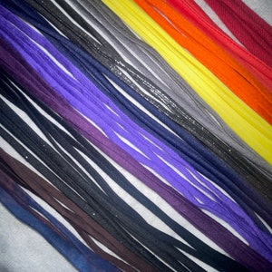 May include: A collection of colorful shoelaces in various shades of red, orange, yellow, gray, purple, and black. The shoelaces are arranged in a diagonal pattern on a white surface.