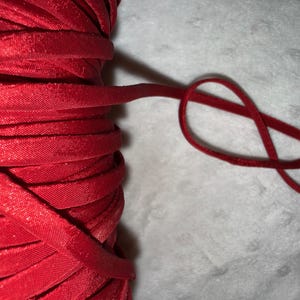 May include: Close-up of a spool of bright red satin ribbon. The ribbon is tightly wound, with a length of the ribbon looped into a figure eight. The ribbon has a smooth, shiny texture, and is suitable for crafts and gift wrapping.
