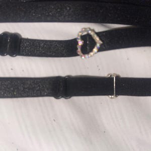 May include: Two black elastic straps with adjustable metal clasps. One strap has a heart-shaped rhinestone embellishment.