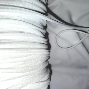 May include: Close-up of a spool of white elastic cord, tightly wound. The cord is smooth and appears to be made of a woven material. A single strand of the cord is looped on a white fabric background.