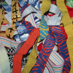 May include: A close-up of a pile of colorful ribbons and elastic bands. The ribbons feature various patterns, including stripes, animal prints, and floral designs. Colors include red, blue, yellow, and green.