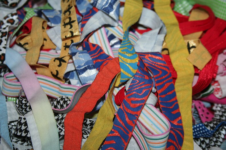 May include: A close-up of a pile of colorful ribbons and elastic bands. The ribbons feature various patterns, including stripes, animal prints, and floral designs. Colors include red, blue, yellow, and green.