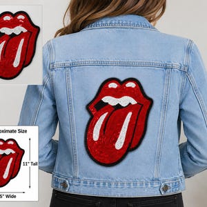 May include: A light blue denim jacket featuring a large, red, white, and black sequined lips and tongue patch on the back. The patch measures 11 inches tall and 8.5 inches wide, as indicated by the included ruler and dimension graphic.
