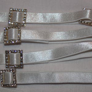 May include: White satin ribbon with multiple rows of rhinestone buckles. The buckles are square shaped and have a silver finish.