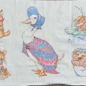 May include: A white fabric panel featuring illustrations of storybook characters. The characters include a rabbit, duck, cat, mouse, and hedgehog, all in pastel colors. The illustrations are reminiscent of children's book art.