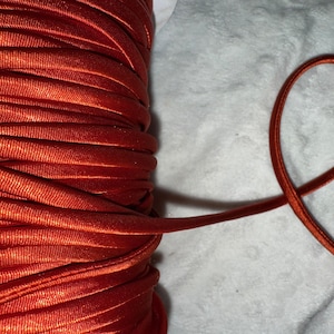 May include: A spool of orange satin cord. The cord is wound tightly and has a smooth, shiny finish.