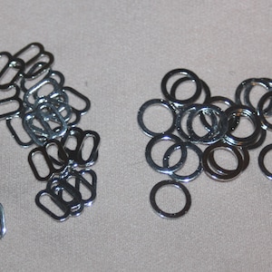 May include: A collection of silver-colored metal rings and rectangular sliders. The rings are circular, and the sliders have two oval openings. These findings are likely used in jewelry making or garment construction.