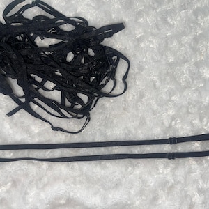 May include: A pile of black elastic straps with two longer straps lying on a white fuzzy surface.