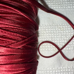 May include: A spool of deep red satin ribbon. The ribbon is wound tightly and has a smooth, shiny finish.