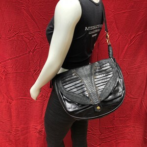 May include: A black leather shoulder bag with a flap closure and a decorative snake skin pattern. The bag has a gold buckle and a long strap.