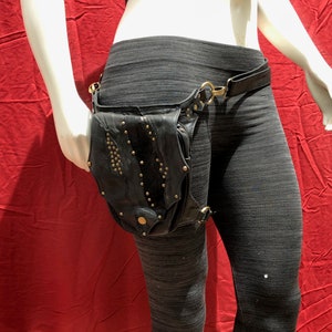 May include: A black leather thigh holster with gold studs and a belt loop. The holster is worn on a mannequin with black leggings.