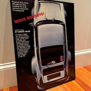 May include: A black and white poster featuring a silver Porsche Turbo Carrera with the text "WAVE GOODBYE!" and "modern living BY BROCK YATES".