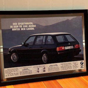 May include: A black BMW station wagon with the text "Der Sportwagen, in dem Sie eine Menge hinter sich lassen."  The car is parked on a road with mountains in the background. The car has a license plate that reads "MXD 5809".
