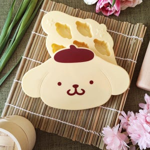 May include: A yellow silicone baking mould shaped like a cartoon dog with a red beret. The mould has six heart-shaped cavities for baking treats.