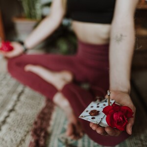 Peut inclure: Une personne tenant une petite assiette blanche avec une rose rouge et un b&acirc;ton d'encens allum&eacute;. L'assiette est sur un tapis &agrave; motifs blancs et bruns.