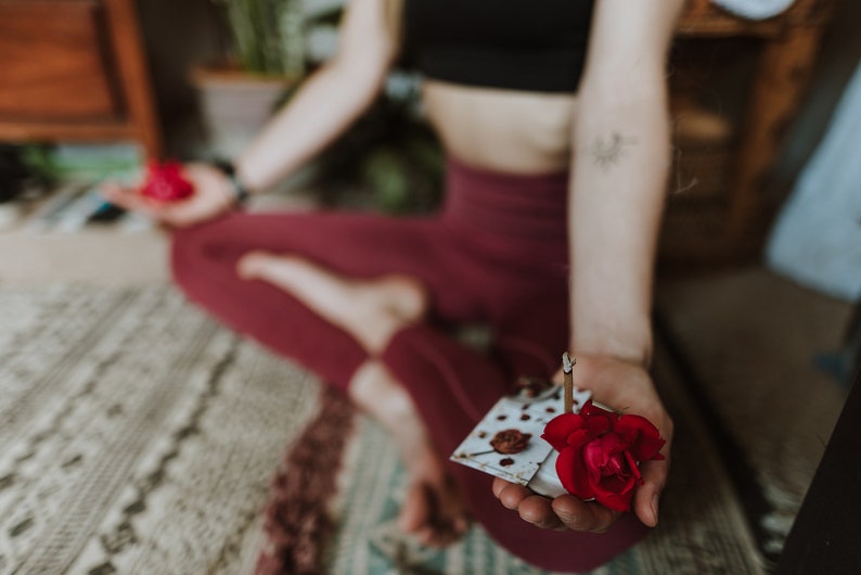 Peut inclure: Une personne tenant une petite assiette blanche avec une rose rouge et un b&acirc;ton d'encens allum&eacute;. L'assiette est sur un tapis &agrave; motifs blancs et bruns.