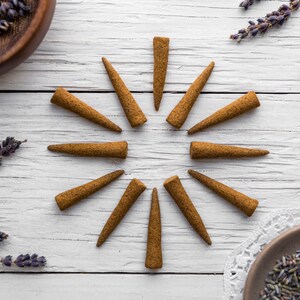 Op de afbeelding: Een set van 12 bruine wierookkegels, gerangschikt in een cirkel op een wit houten oppervlak. Gedroogde lavendeltakjes zijn rond de kegels verspreid.