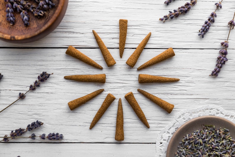 Op de afbeelding: Een set van 12 bruine wierookkegels, gerangschikt in een cirkel op een wit houten oppervlak. Gedroogde lavendeltakjes zijn rond de kegels verspreid.