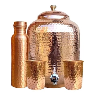 May include: A copper water set featuring a hammered texture. The set includes a water bottle, a large water dispenser with a spigot, and two drinking glasses. The copper has a warm, reddish-brown hue.