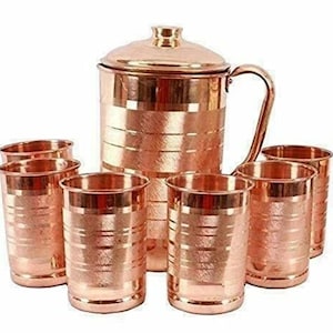 Op de afbeelding: Een koperen kan met deksel en handvat, vergezeld van zes bijpassende koperen drinkglazen. De set heeft een glanzende, metalen afwerking en een traditioneel ontwerp. De glazen zijn ongeveer 10 cm hoog.