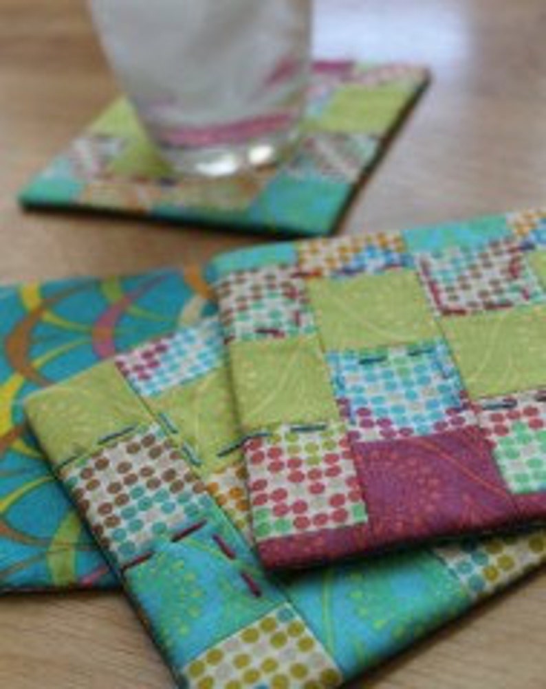 Puede incluir: Cuatro posavasos de tela hechos a mano en una variedad de patrones y colores, incluyendo verde, azul, rosa y marr&oacute;n. Los posavasos est&aacute;n hechos de cuadrados de tela patchwork y tienen un dise&ntilde;o acolchado.