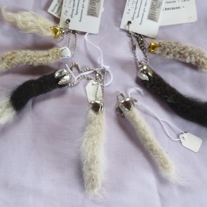 May include: Keyrings with small, furry animal tails in shades of black, white, and beige. Each tail is attached to a silver-tone metal charm and chain. Small tags are attached to the keyrings.