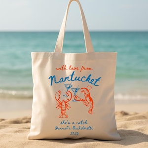 Puede incluir: Bolso tote de color crema con temática playera. El bolso presenta el texto "with love from Nantucket" en rojo y azul, junto con ilustraciones de langostas y cócteles. El texto adicional dice "she's a catch Hannah's Bachelorette 2026".