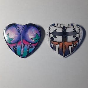 May include: Two heart-shaped buttons. One features a purple and blue galaxy design with green stars and the word "TITS" in teal. The other has a white background with a cartoon character, a sword, and the word "TITS" in orange and blue.