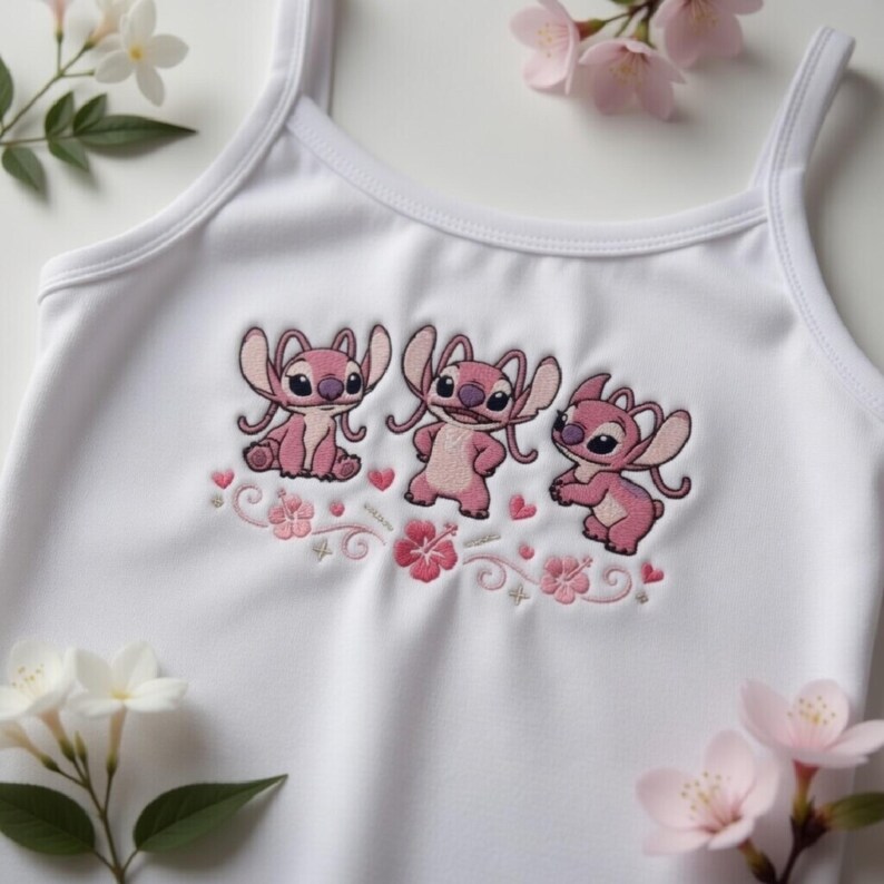 May include: White tank top featuring an embroidered design of three pink cartoon characters with large ears. The design includes pink flowers and hearts. The tank top has thin straps.