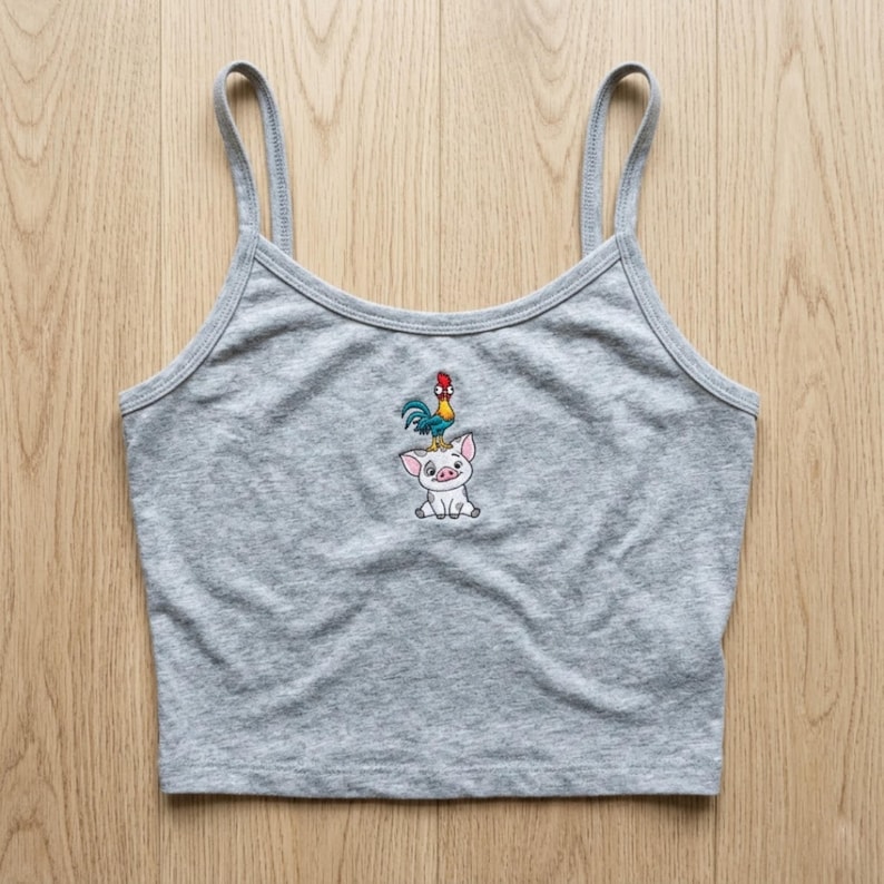 May include: A gray crop top with thin straps. The top features an embroidered design of a pig with a rooster on its head. The design is in shades of blue, red, yellow, and white. The top is made of a soft, comfortable material.